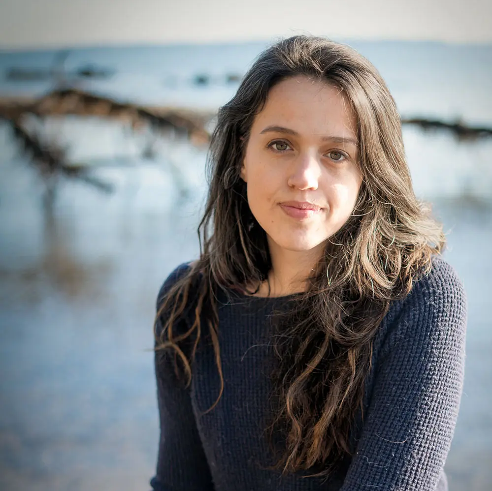 Photograph of a white woman with long brown hair wearing a black shirt looking into the camera.