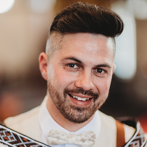 Photograph of a man with fair skin, short brown hair, and brown eyes smiling to camera.