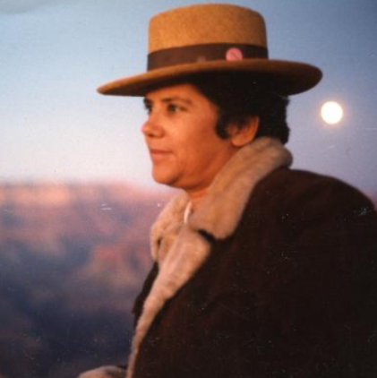 Photograph of Jeanne Córdova staring into the distance, wearing a beige hat and dark brown jacket.