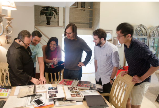 Photograph of people leaning over a table looking at photographs in binders
