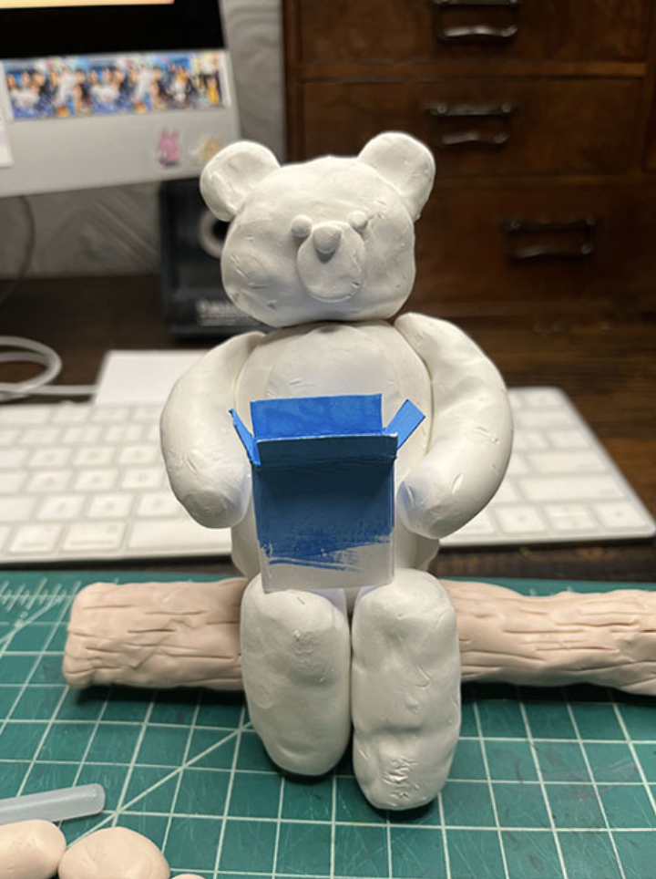 Photo of a bear built of clay holding a blue box