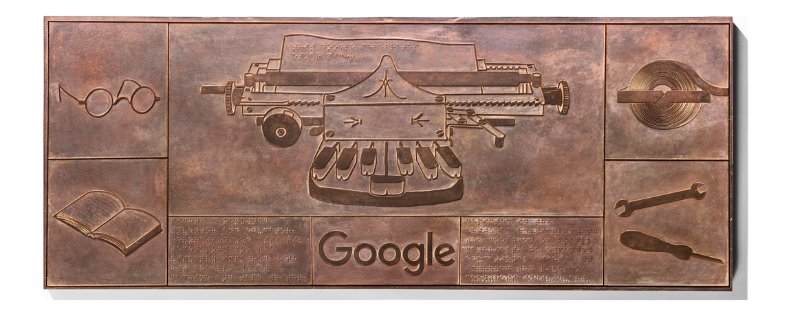 Photograph of the Doodle which is bronze relief showing a typewriter, braille, Google, and other symbolism. 