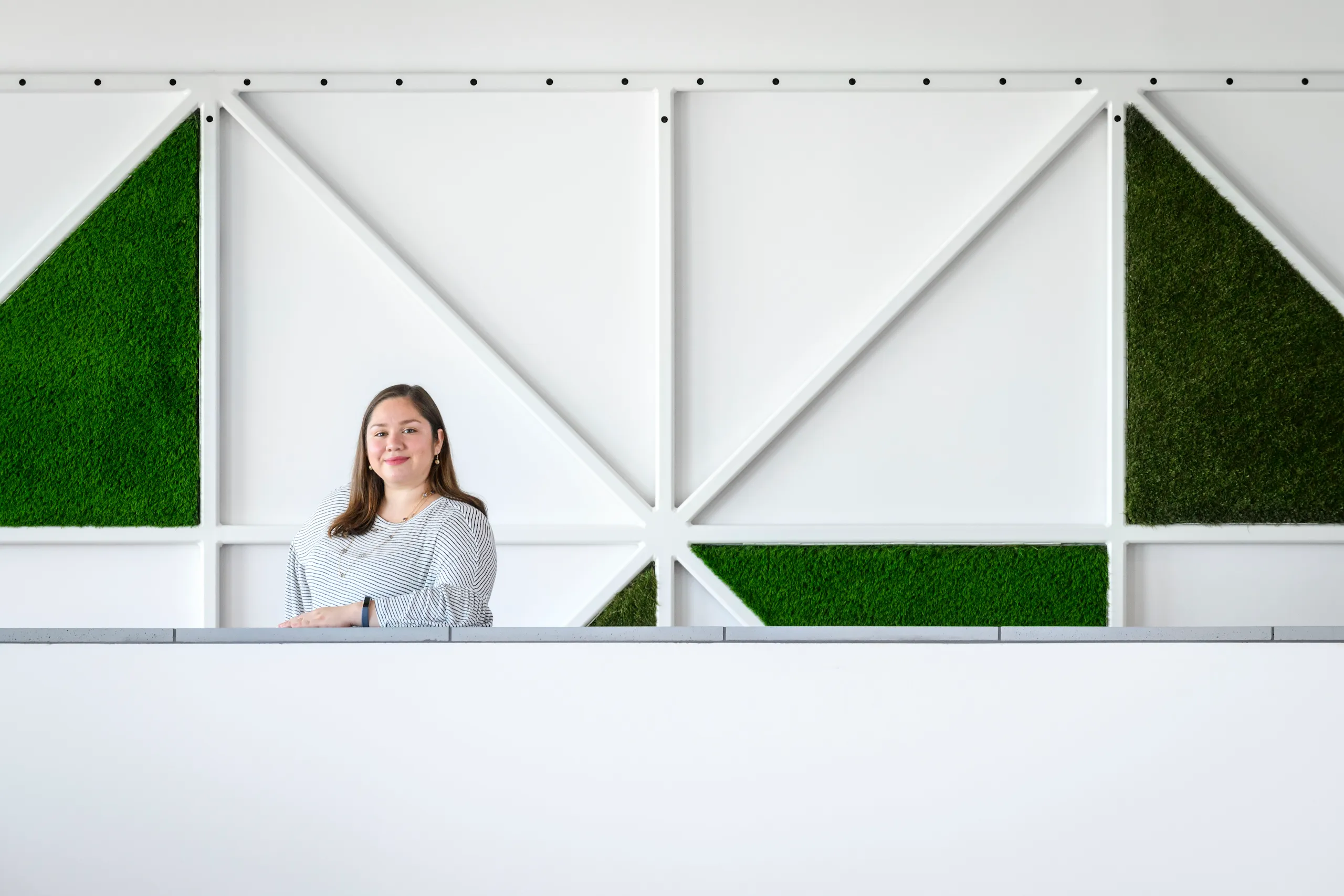 Photograph of a woman smiling with arm on ledge standing in front of a graphic wall background.