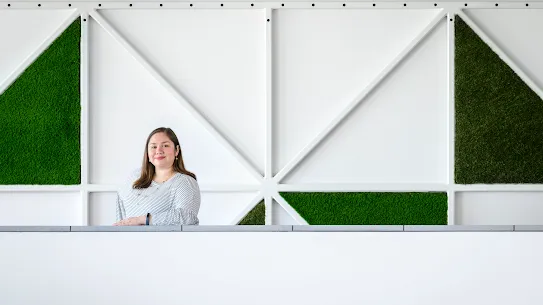 Photograph of a woman smiling with arm on ledge standing in front of a graphic wall background.