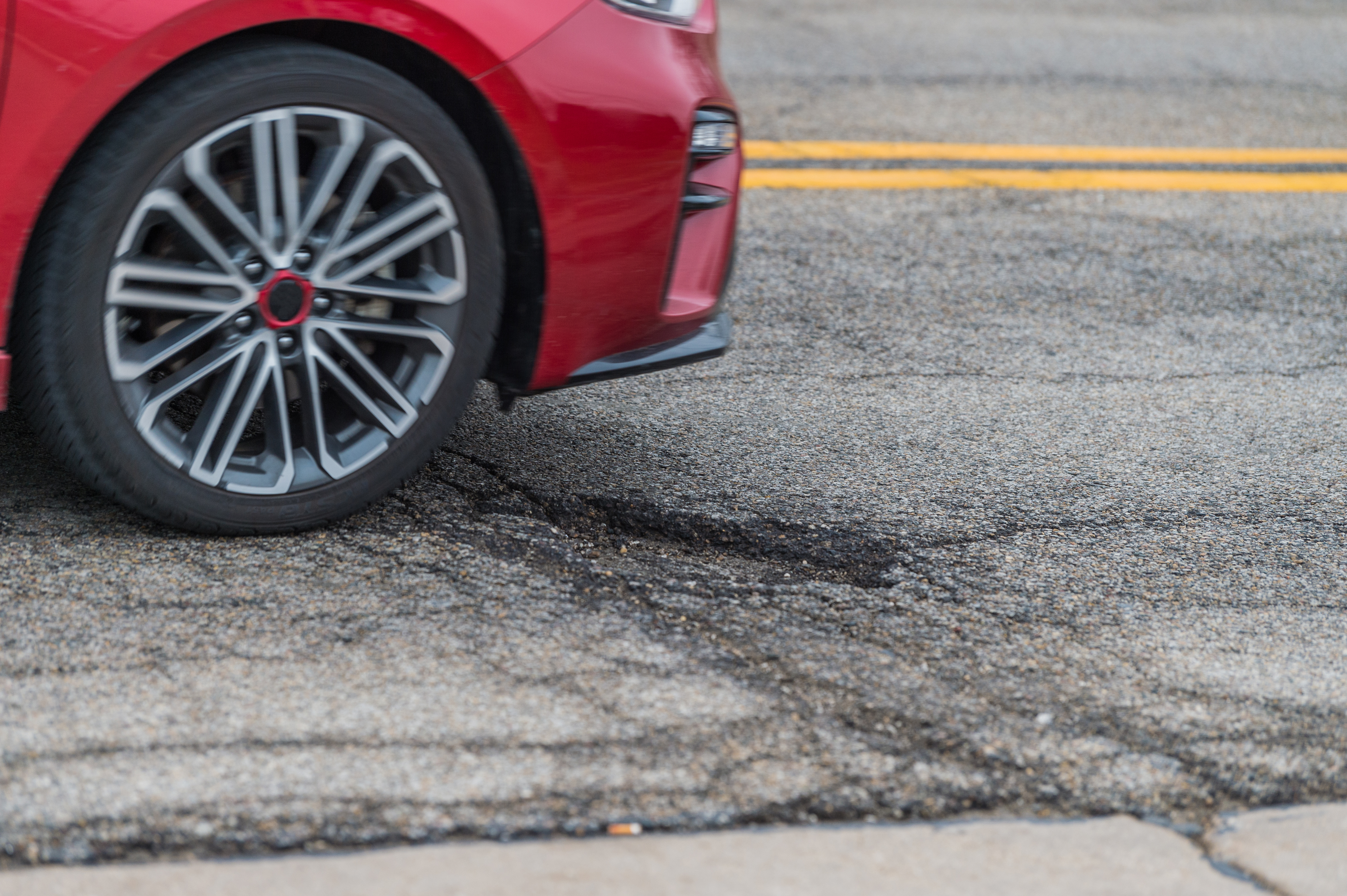 Red car driving over a pothole on a city street