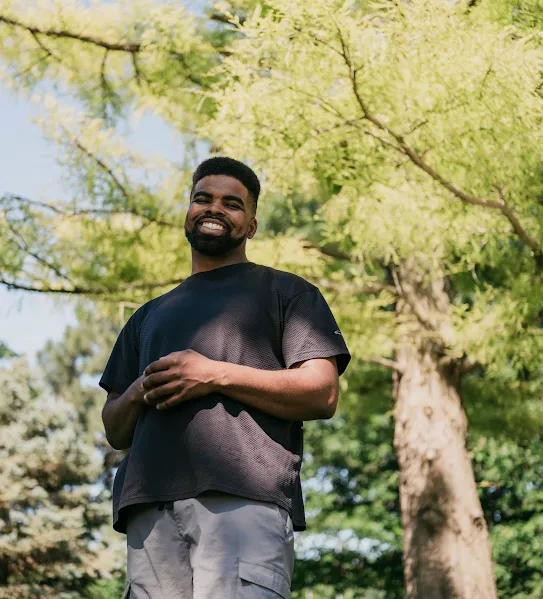 A recent Google Skilled Trades and Readiness Program graduate stands outside under the trees, smiling.