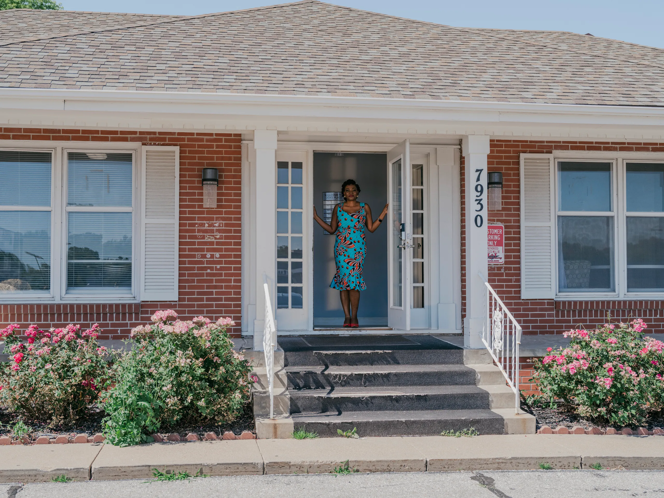 Karine Sokopoh stands in the doorway of a brick building on a sunny afternoon