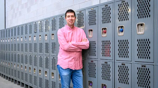 Photograph of a man with arms crossed standing against lockers in a Google facility.