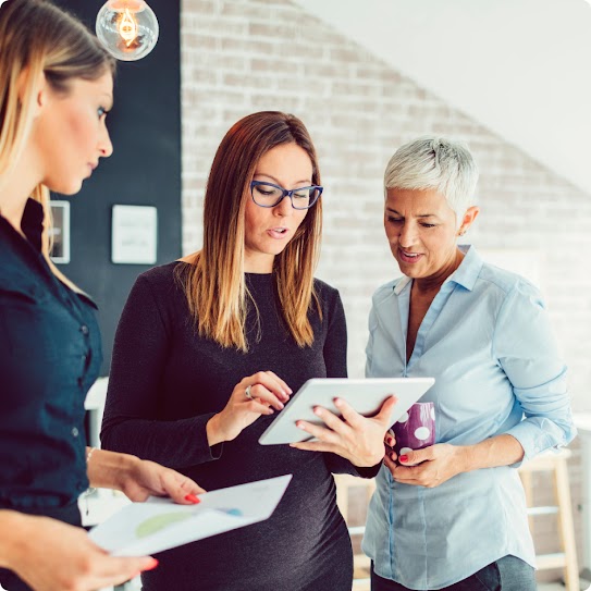 Ein diverses Team steht beieinander, schaut gemeinsam in eine Arbeitsmappe und betrachtet deren Inhalt.