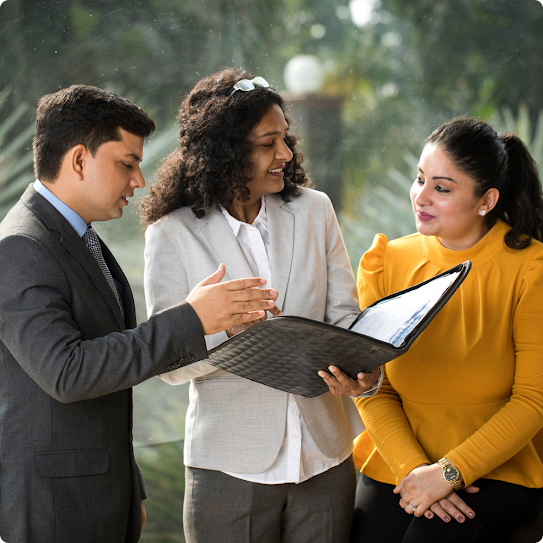 A diverse team huddles around one team member holding an open file and reviewing its contents.