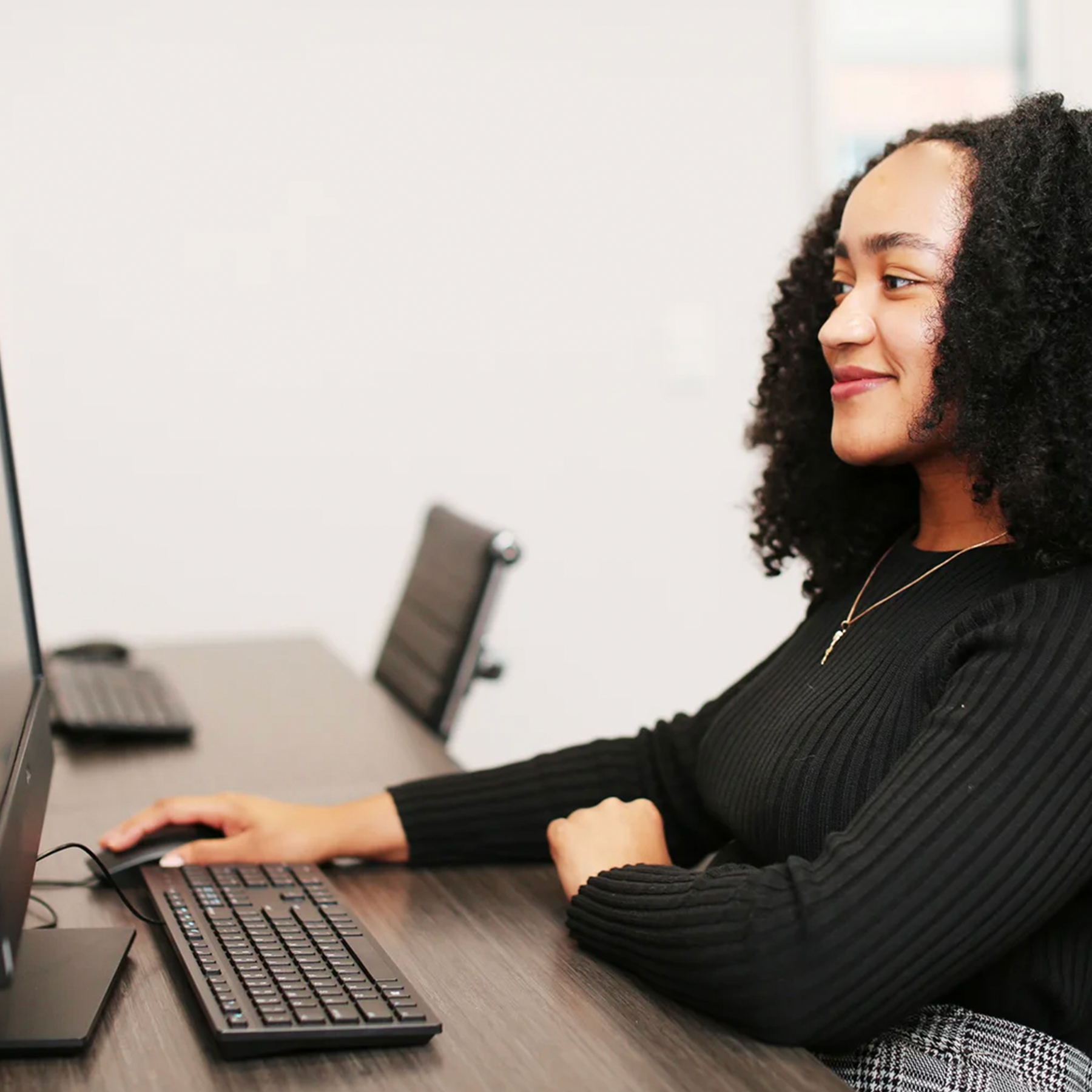 A young, smiling woman sits at a computer in front of a sunny window at the University of Georgia's cybersecurity clinic.