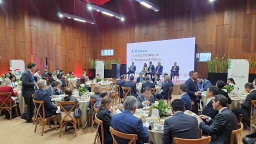 Groups of people sitting around tables in front of a stage with a panel of speakers