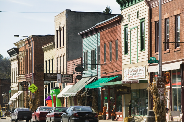 Line of storefronts on a small town street with cars parked along the road side