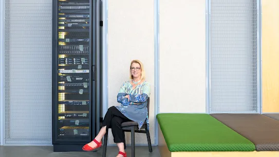 Photograph of a smiling woman with arms and legs crossed sitting in a chair in a Google facility.