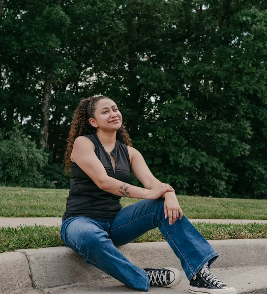 A recent Google Skilled Trades and Readiness Program graduate sits outside on the curb, smiling.