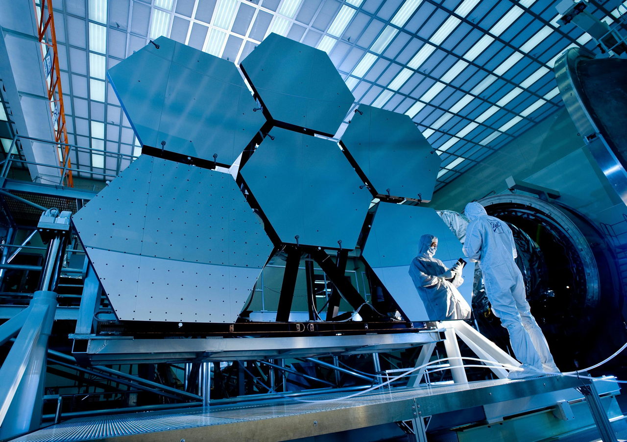 high angle view of a man wearing a white body suit and looking a tablet in front of a piece of equipment