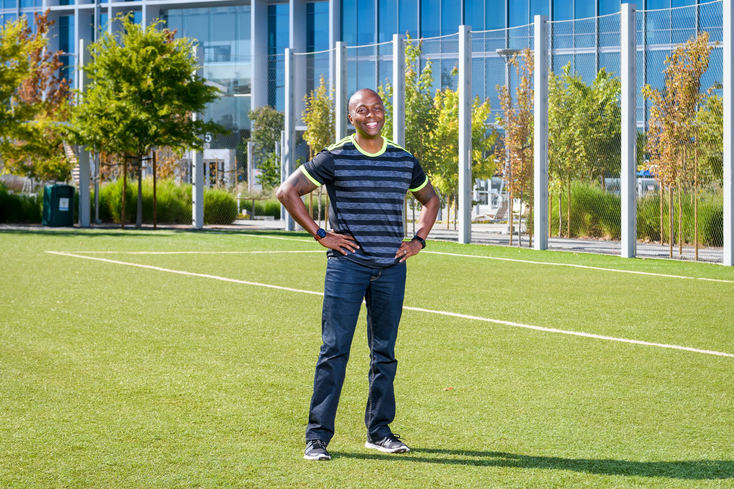 Photograph of a smiling man standing on a field with hands on hips.