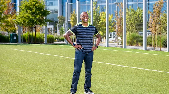 Photograph of a smiling man standing on a field with hands on hips.