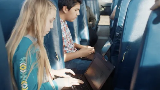 Kids work on their laptops while sitting in the school bus