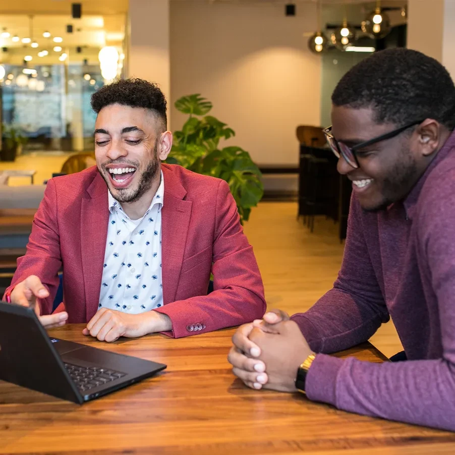 Two colleagues seated in an office setting discuss a presentation on a laptop