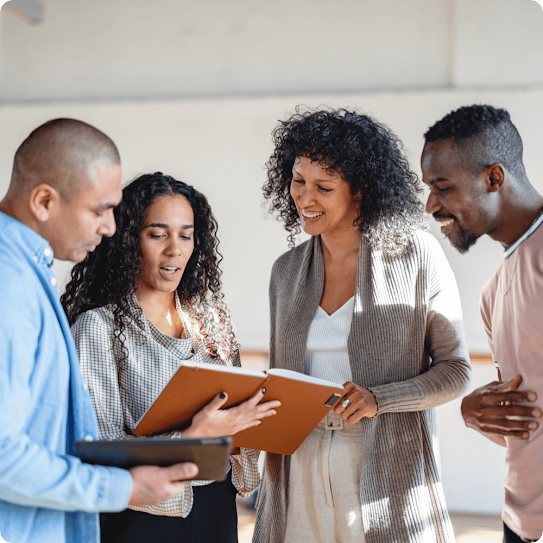 A diverse team huddles around one team member holding an open file and reviewing its contents.