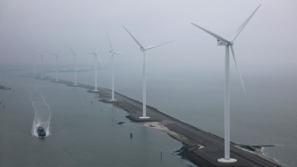 Turbinas eólicas cerca del agua, situadas a lo largo de una delgada franja de tierra en un clima con niebla.