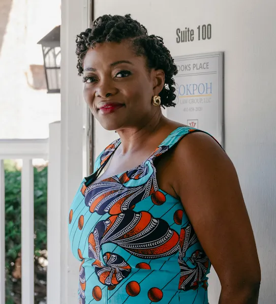 The founder of a non-profit organization that supports local residents, the woman in a colorful dress stands outside a brick building and smiles.