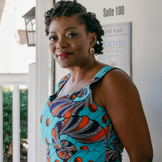 The founder of a non-profit organization that supports local residents, the woman in a colorful dress stands outside a brick building and smiles.