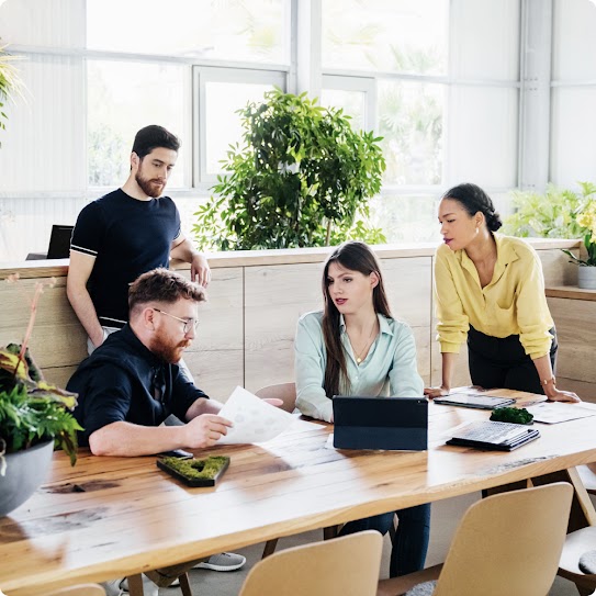 A diverse team huddles around one team member holding an open file and reviewing its contents.