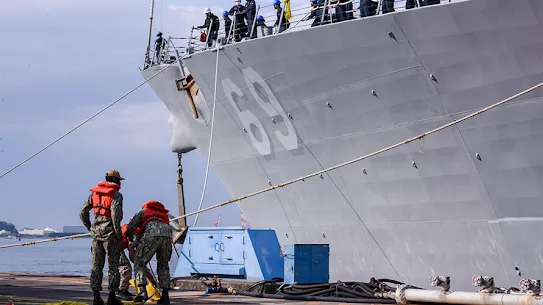 Soldiers in camouflage gear on a navy vessel during operations.