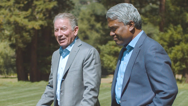 Photo of Tom Siebel and Thomas Kurian shaking hands in front of a green field