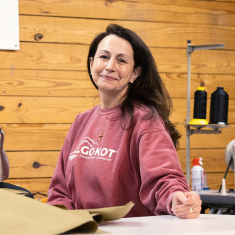 Woman with dark shoulder length hair wearing a light pink sweatshirt sits at a workstation with a sewing machine