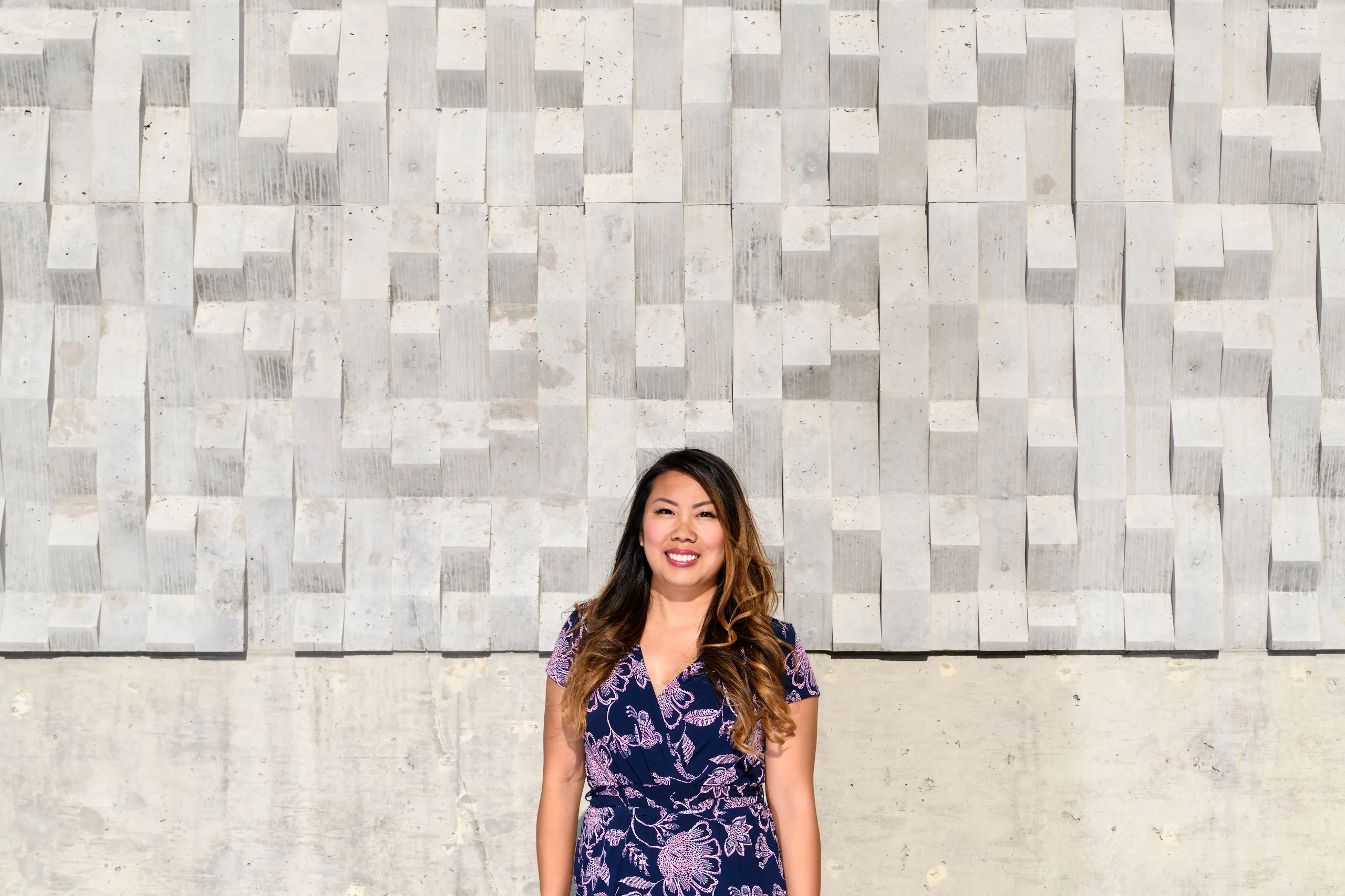 Photograph of a woman smiling standing in front of a textured wall.