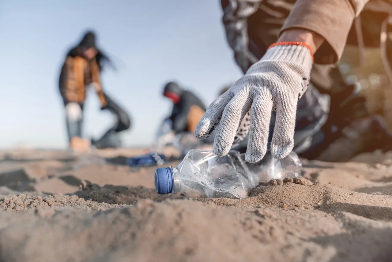 Una persona recoge una botella de agua de plástico en una playa de arena