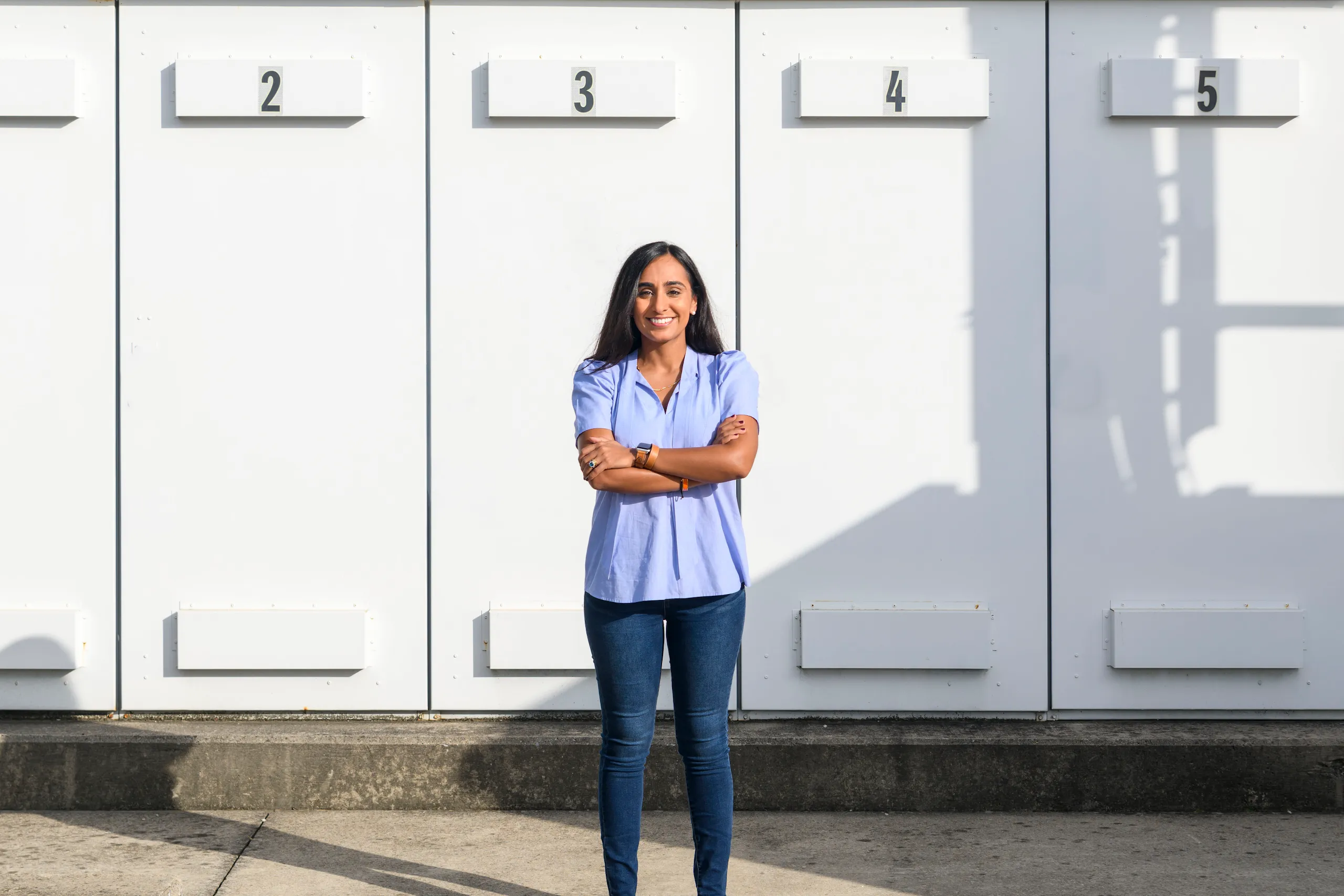 Woman in blue shirt stands with arms crossed at center of photograph