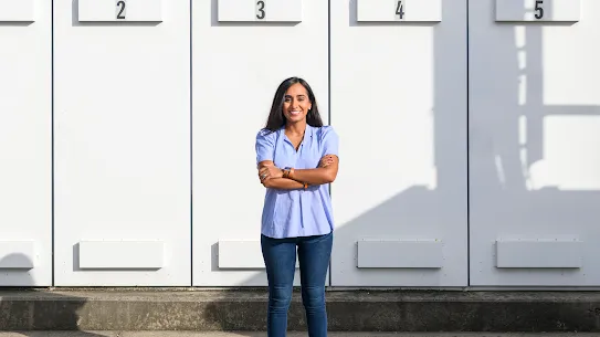 Woman in blue shirt stands with arms crossed at center of photograph