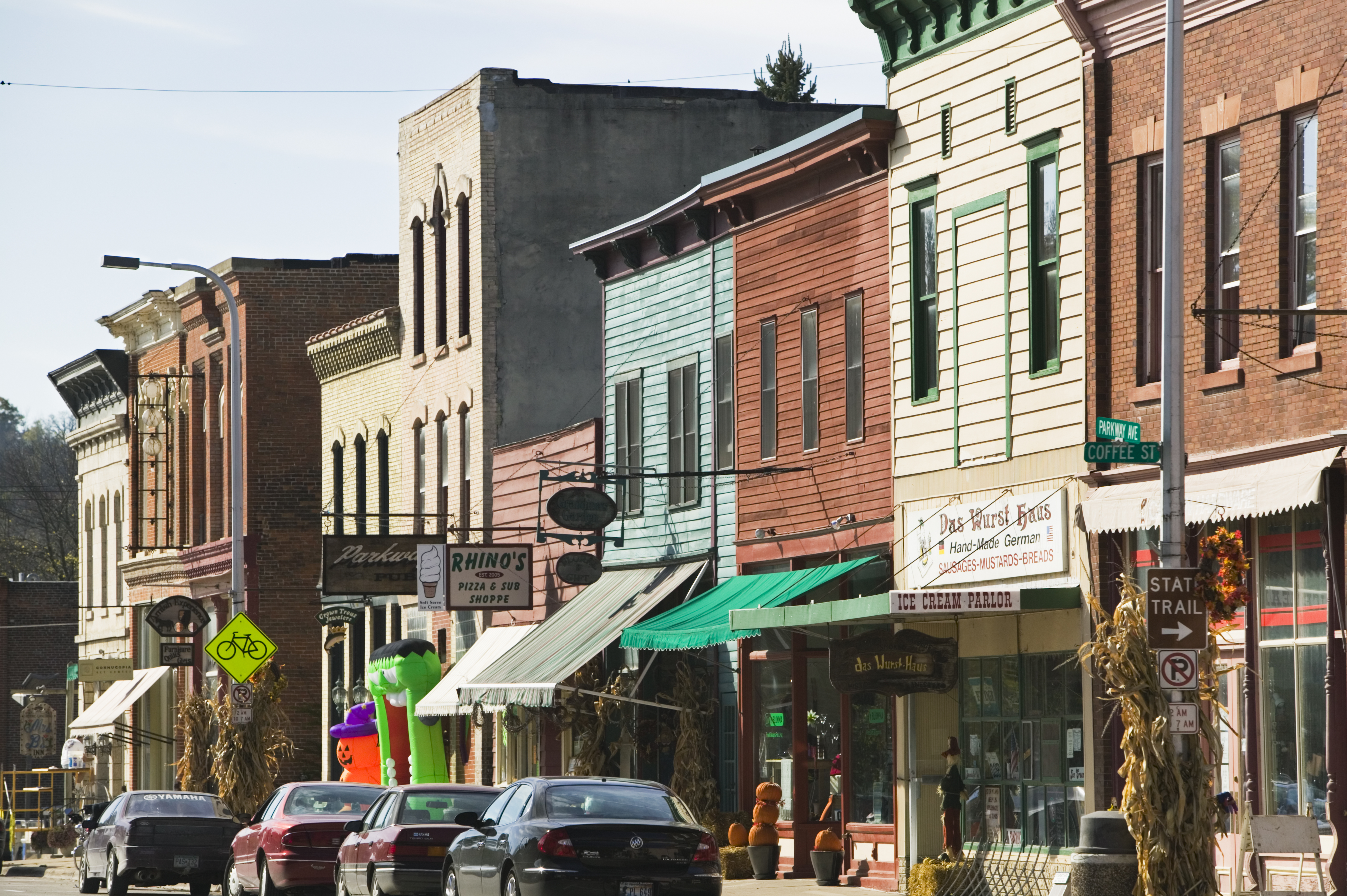 Line of storefronts on a small town street with cars parked along the roadside