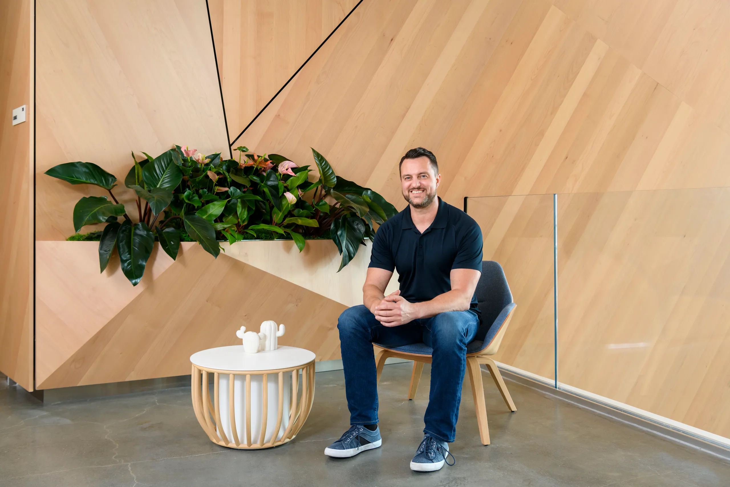 Photograph of a smiling man sitting in a chair in a room with wood paneling. 