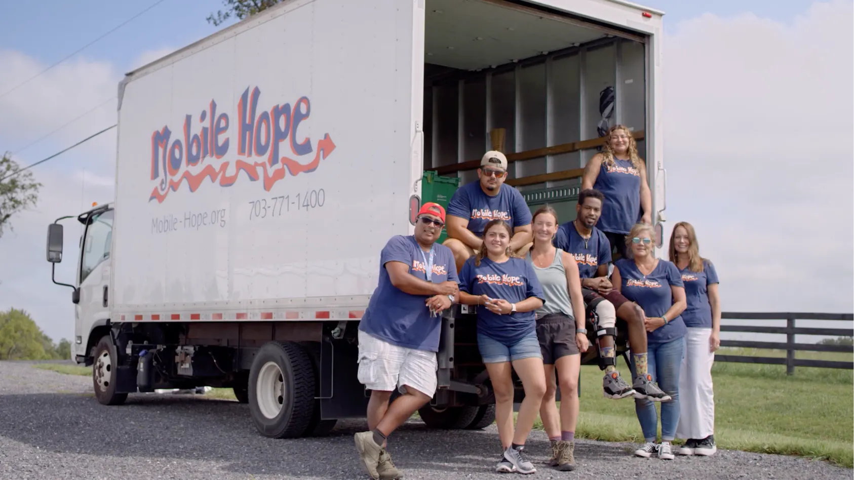 A group of volunteers posing in a group on the back of a box van with Mobile Hope painted on the side. 