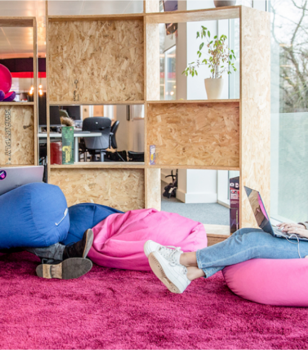 A man, on the left,  and a woman, on the right, sit on blue and pink bean bag chairs in the Octopus Energy office while working on laptops.