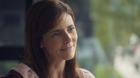 A seated woman with shoulder length brown hair smiles off camera.