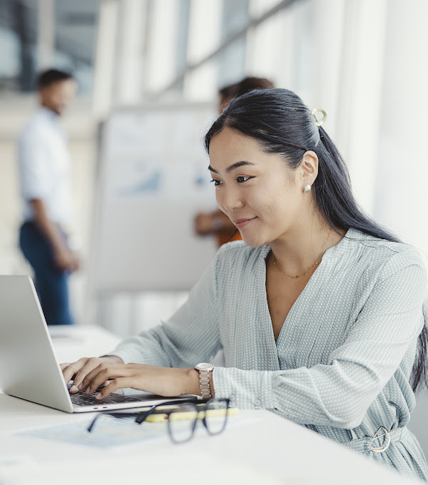 Businesswoman busy working on laptop computer at office with colleagues in the background.