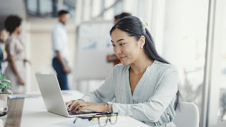 Businesswoman busy working on laptop computer at office with colleagues in the background.