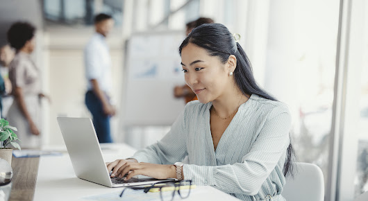 Businesswoman busy working on laptop computer at office with colleagues in the background.