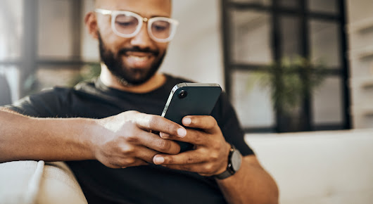 Smiling man using mobile phone while on sofa.