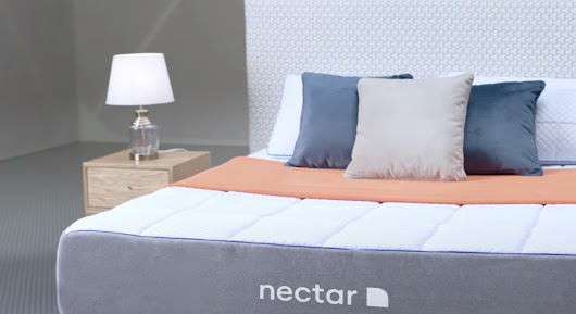 A Nectar bed in the center of a neutral colored room flanked by side tables with lamps.