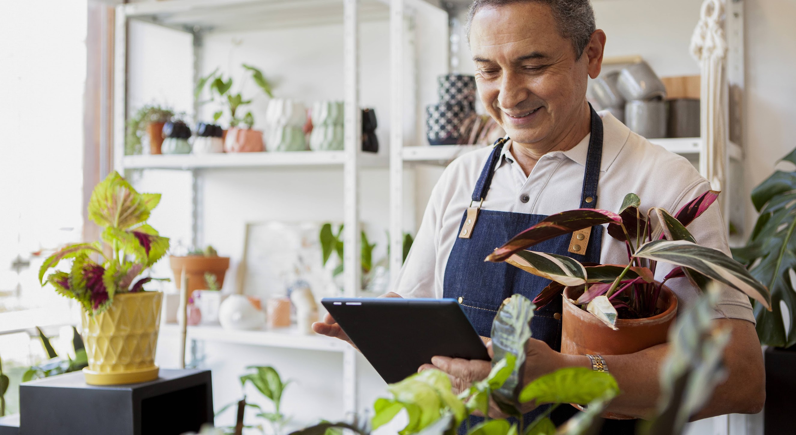 A garden store employee behind a counter with a counter with a tablet in his hand.