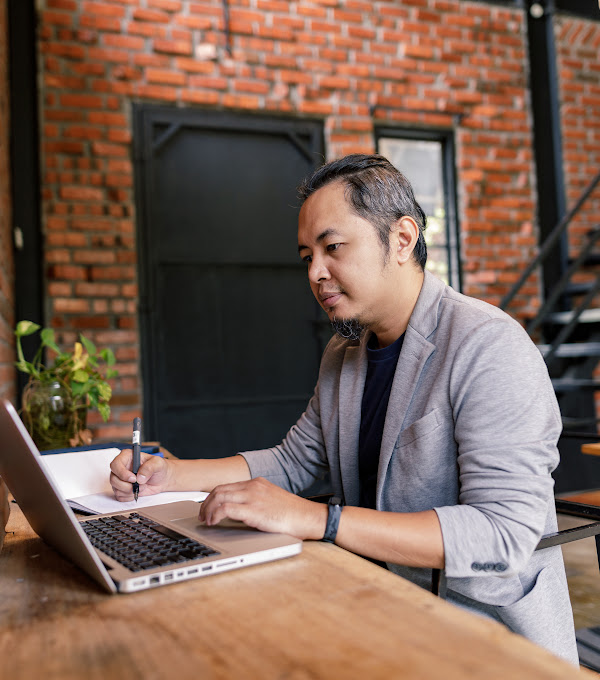 Portrait of a man writing down details from his laptop.