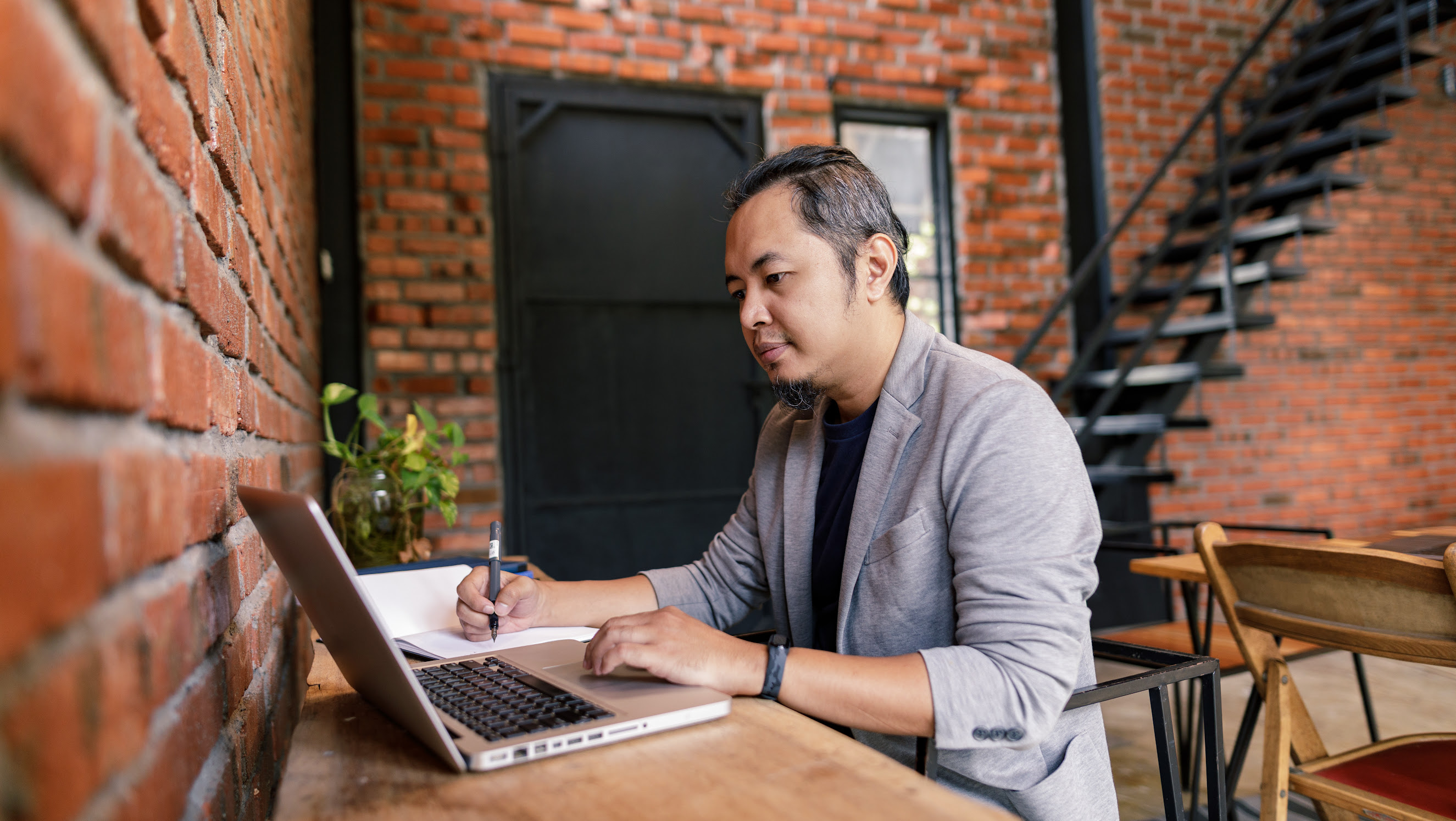 Portrait of a man writing down details from his laptop.