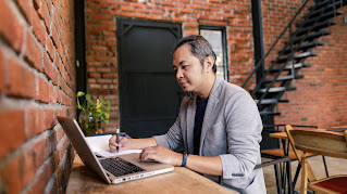 Portrait of a man writing down details from his laptop.